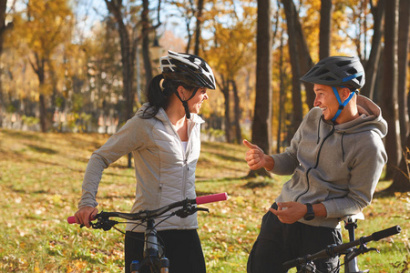 快乐的年轻夫妇有乐趣骑自行车在阳光明媚的秋季天在公园里