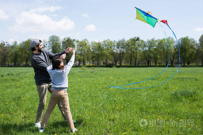 微笑的父亲和女儿在公园的草地上放飞风筝