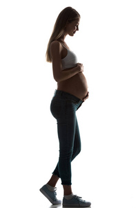 怀孕的妇女剪影接触她的腹部查出的白色