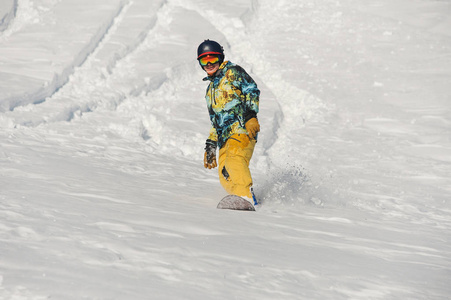 活跃的年轻滑雪板在橙色运动服骑下雪山在明亮的冬天对白雪
