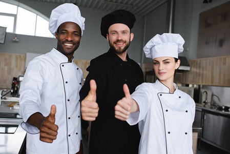 微笑的多文化的厨师在餐馆厨房显示竖起大拇指