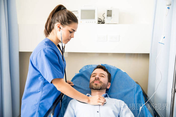 漂亮的护士用听诊器检查在医院病房的男性病人