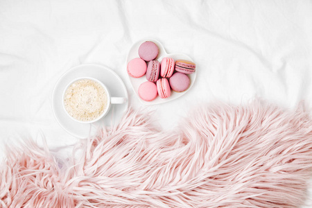 杯咖啡和马卡龙在盘子上粉红色蓬松羽绒被