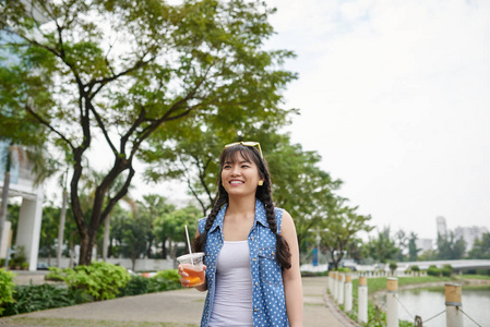 微笑的越南妇女用塑料杯子冰茶走在街道