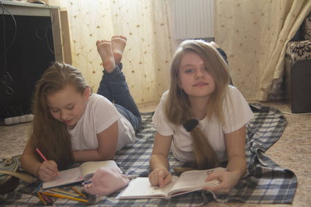 两个十几岁的女孩, 他们花时间在家看书和画画, 而躺在地板上