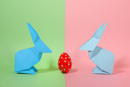 折纸纸五颜六色的兔子与鸡蛋在两个色调的背景。复活节想法