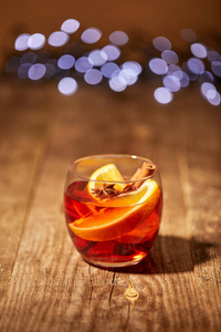 在散景灯的背景下, 在木质表面上的橙色片和八角星的葡萄酒饮料的特写视图