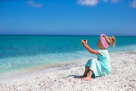 可爱的小女孩拍照手机在地处热带的海滩上