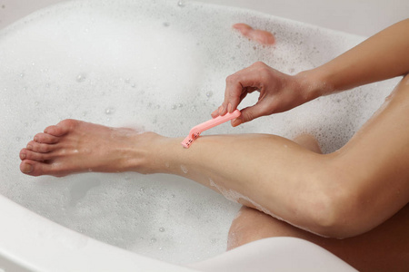 女人用水和泡沫在浴缸里剃她的腿