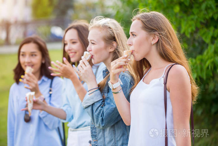 照片 四快乐的年轻女友站在一排微笑着愉快地在公园吃冰淇淋.