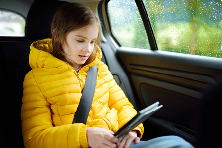 可爱的女孩坐在汽车和阅读她的电子书在下雨的秋天天。儿童娱乐 herserf 在路上旅行。开车和孩子们一起旅行