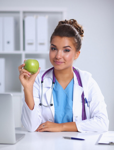 一位女医生手拿着一个绿色的苹果，坐在办公桌前