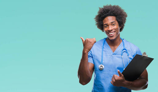 美国黑人外科医生拿着剪贴板人在孤立的背景指向和显示与拇指到一边, 快乐的脸微笑着
