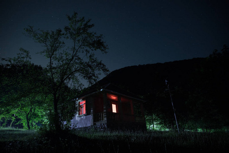 晚上在森林里建筑的山夜风景与月亮或老式乡下房子在晚上与云彩和星。夏日之夜。照片拍摄与长期曝光