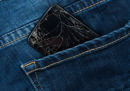 在蓝色牛仔裤口袋里有一个破碎的屏幕的手机