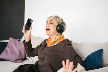 一位积极的老年妇女听音乐和唱歌。老一辈和新技术