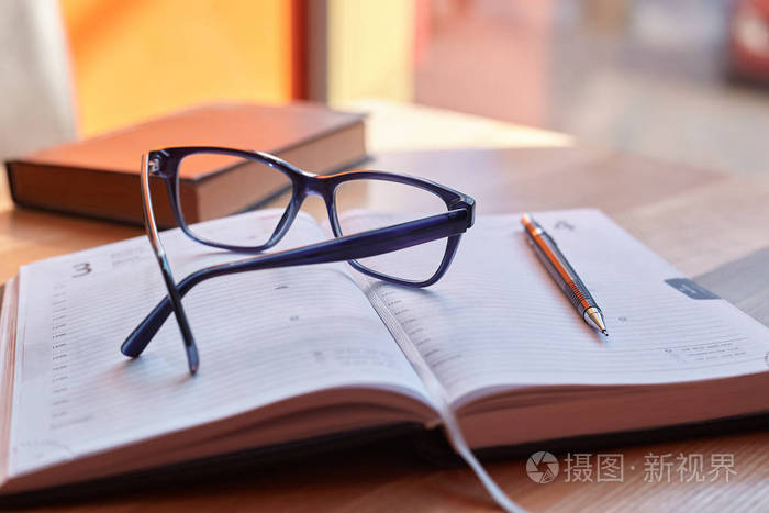 在一本书旁边的木桌上的一张纸上的眼镜和一支钢笔