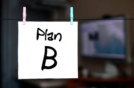 计划 b. 注释写在一个白色的贴纸上, 上面挂着一个 clothespin 在办公室内部的背景上的绳子上。