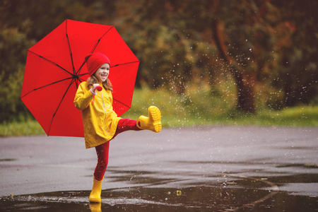 快乐的孩子女孩用雨伞和橡胶靴跳在水坑上的秋季沃尔玛