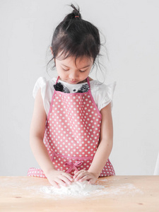 快乐亚洲女孩粉红色围裙准备面粉饼干或比萨饼面团, 生活方式概念