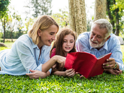 家庭父亲母亲和女儿的活动在公园里躺着绿草的时候看书。