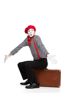 mime 坐在棕色手提箱和显示耸耸肩手势隔离白色