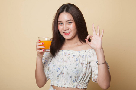 年轻的亚洲妇女喝橙汁显示 Ok 标志米色背景