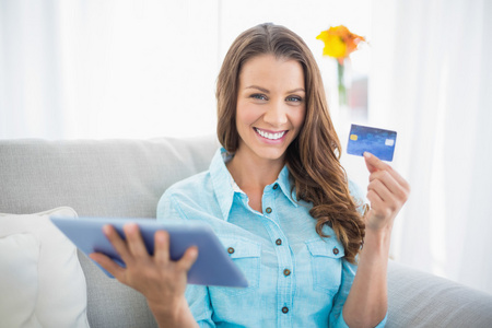 微笑的女人举行平板和显示她的信用卡
