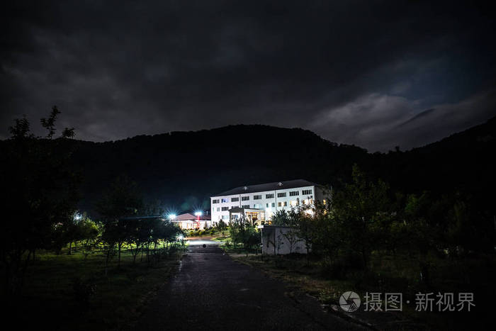 晚上在森林里建筑的山夜风景与月亮或老式乡下房子在晚上与云彩和星.