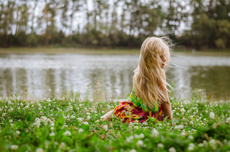 长头发的小女孩坐在河的草