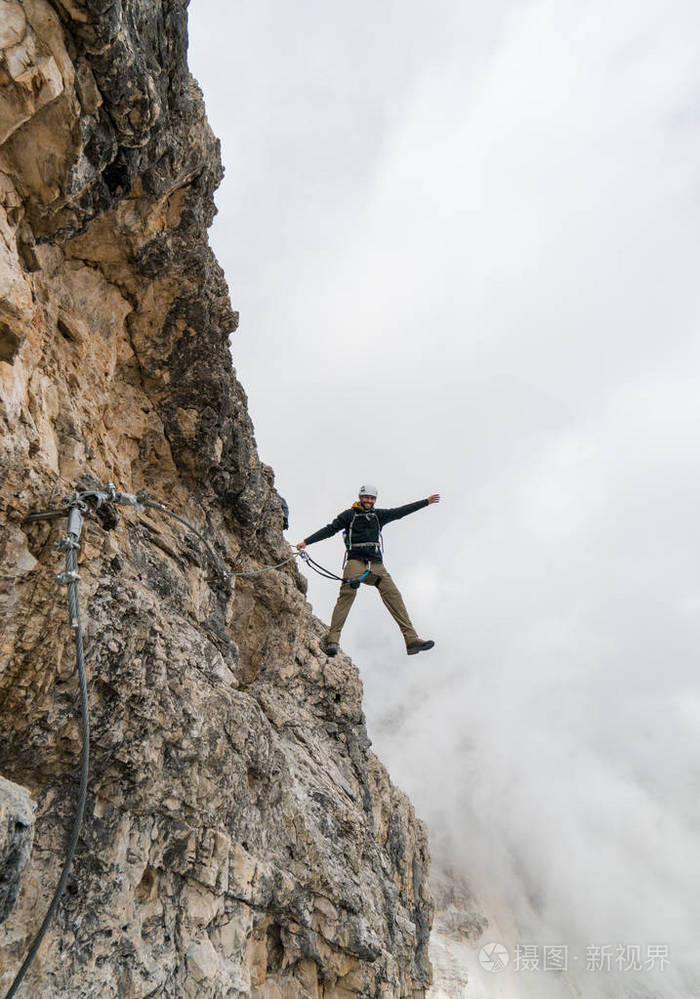 在陡峭和裸露的岩石面上攀爬的年轻男性登山者通过ferrata