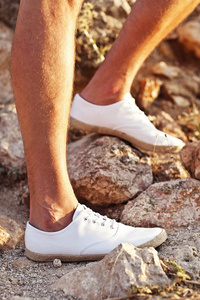男人的腿在石路上的白色网球鞋。