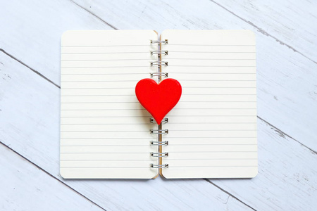 在白色木制背景上打开书上的红色木制手工心脏符号的顶部视图。情人节主题