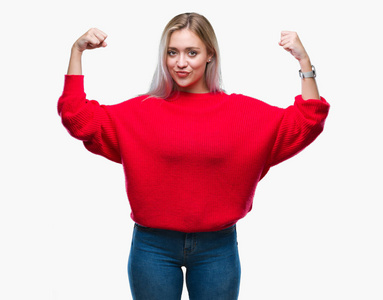年轻的金发女人穿着冬季毛衣在孤立的背景下显示手臂肌肉微笑自豪。健身理念