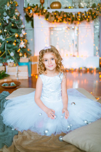 可爱的小女孩, 金色卷发在家里附近的圣诞树与礼品和花环和装饰壁炉坐在格子和枕头