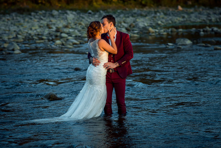 Hroziontal 婚礼拍摄的迷人的新婚夫妇亲吻 whwile 站在河中的日落