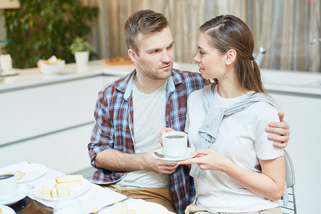 年轻人拥抱他的妻子与杯茶在早餐和她说话