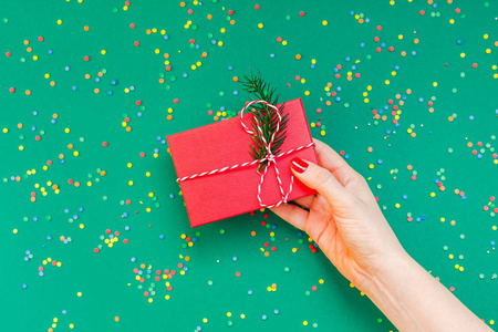 新年或圣诞顶级景观圣诞假期庆祝妇女手红色指甲持有礼物盒复制空间绿色纸张背景。模板贺卡
