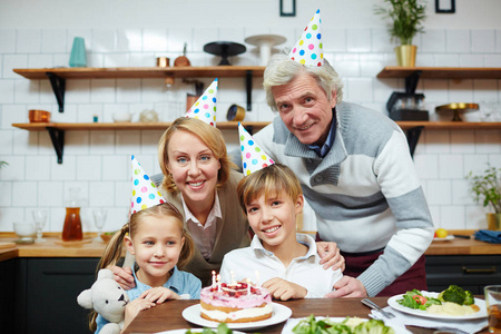 可爱的孩子和他们的祖父母在生日帽子坐在节日桌