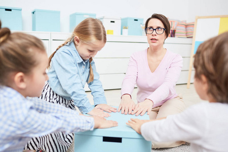 老师和她的幼稚园小组保持他们的 h 在蓝色箱子的顶部在戏剧期间