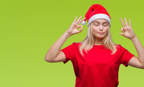 年轻的白种女人戴着圣诞帽子在孤立的背景下放松和微笑与眼睛关闭做冥想手势与手指。瑜伽概念