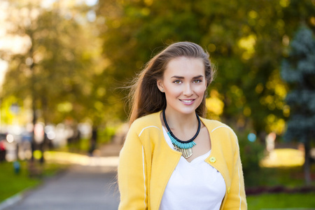 幸福的年轻女人在黄色的外套，在秋季街头