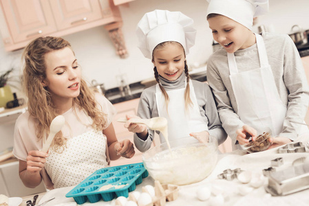 母亲教她的孩子用白帽子在厨房准备饼干