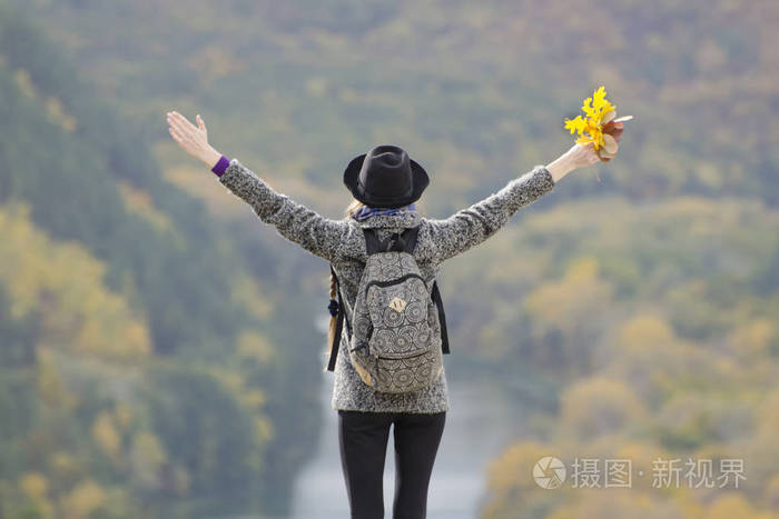 一个背包和一顶帽子站在山上的女孩.举手.下面是河流和山脉.后视图
