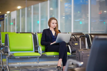 国际机场的年轻女子在等待她的航班时在笔记本电脑上工作