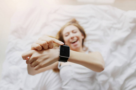 关注 smartwatches 显示年轻女子躺在白色的床上