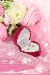毛茛属 波斯毛茛属植物 和粉红色的布上的订婚戒指