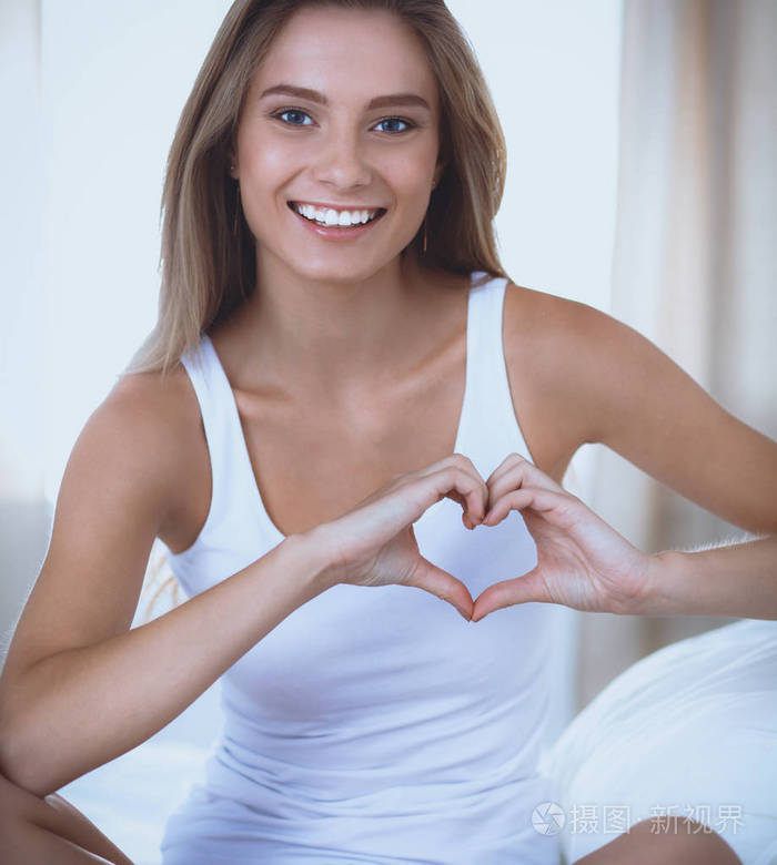 美丽的女人心的形状显示在她的手坐在床上