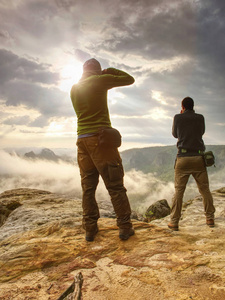 徒步旅行者和摄影师留在悬崖上拍照。秋天的自然, 朦胧的景色多云的天空