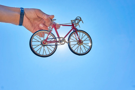 红色金属玩具自行车在手上的背景晴朗的天空和太阳在晴朗晴朗的一天在夏天旅行时